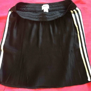  - Superfin kjol i tunt material som är ”veckat”, se bilder.    Svart med 3 vita ränder på sidorna. Mudd upptill. Köpt förra året men helt oanvänd av mig så i nyskick. 