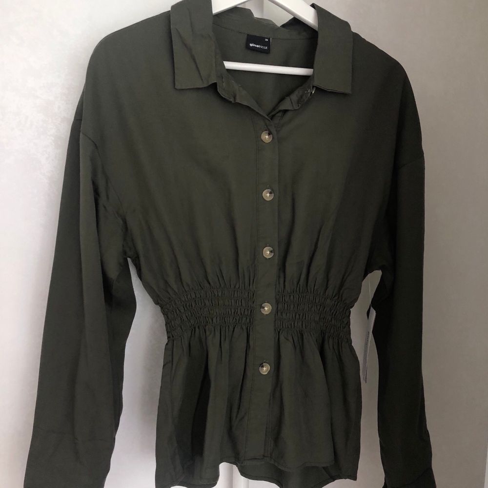 En militärgrön skjorta från Gina Tricot med smock detalj i midjan, för att skapa en fin figur. Strl 36. Helt oanvänd med prislapp kvar. Köpt för 350kr men säljer för 250kr + frakt. Önskas fler bilder är det bara att hojta till🌸. Skjortor.