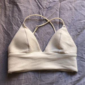 Bikiniöverdel, vit, ribbad - Vit bikiniöverdel som är ribbad och har korsade justerbara band på ryggen. Tjockare band under luvorna. 