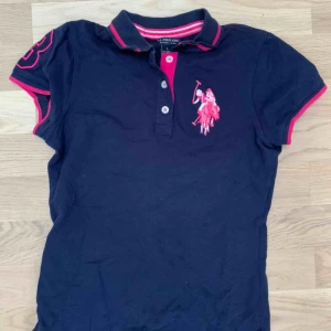  - Piké tröja, marin blå med rosa detaljer, köparen står för frakten. Kan mötas upp