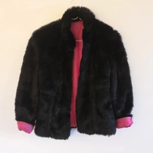  - Second hand, mycket gott skick, fodrad fejk-päls, kort jacka, svart "päls" med cerise foder. Passar XS el. 34