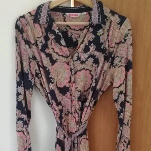  - Fin rosa/aprikos mönstrad skjortklänning på mörkblå botten i stl L från Indiskan. Obetydligt använd. Djur finns i hemmet.  Kan skickas mot att köparen står för frakten.