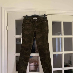  - Jeans i kamouflagemönster med ribbade knän och dragkedjedetaljer. Använda 2 gånger. Frakt tillkommer