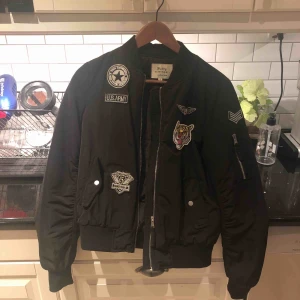  - Svart bomberjacka med patches på