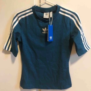  - Blå glittrig adidas originals T-shirt i elastiskt men lite hårdare material. Jättefin på! 