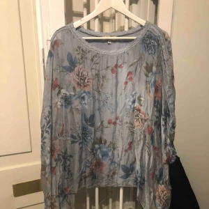  - Blå silkestunika med brodyrrevärer på armarna och öppna axlar. Hela tunikan har samma färg, det är ljuset från lampan som gör att det ser ut som den skiftar.  Använd ett par tillfällen.