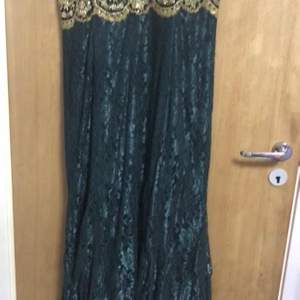 En mörkgrön klänning med guldetalier. Klänningen är använd 1 gång och har storleken 44-46