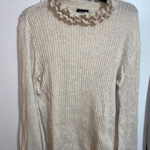 Ljusbeige tröja - En ljusbeige ribbad tröja från bubbleroom. Den har en volangkrage runt halsen samt något vida/ballongärmar. Strl xs men passar även s.