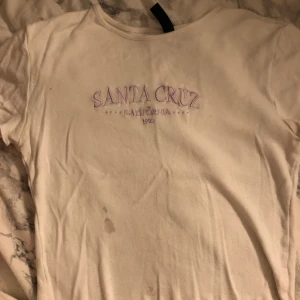 Babytee med text - Vit babytee med lila text i strl XS. Liten fläck på framsidan, säljs därför billigt. Skriv om du vill ha bättre bilder på plagget, tex passform på kroppen osv!