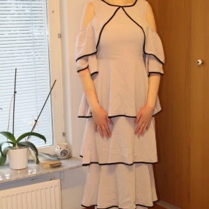 Volang aftonklänning - OBS! Bilderna beskärs på Plick så skriv privat för hela bilder! 😃 Beigerosa klänning med volanger och svarta detaljer. Aldrig använd och prislapp sitter kvar. Strl M/L. Möts upp eller fraktar, skriv privat för fraktkostnaden.
