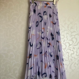 Monki kjol storlek 34 - Lila-mönstrad plisserad midi (halvlång) kjol från monki i storlek 34/XS. Helt ny och aldrig använd, lapparna sitter kvar. Nypris 250kr