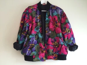  - Färgglad, blommig jacka i bombermodell. Storlek M, men passar bra för en S eller XS. Trasig dragkedja.