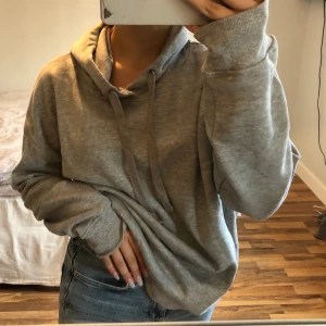 Grå hoodie  - Säljer denna grå hoodie då den inte kommit till användning hos mig. Storlek L men passar även mindre. Tröjan har en mudd nedtill som inte syns så tydligt på bilderna! Frakt tillkommer