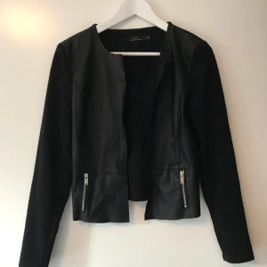  - Tunn jacka med faux-läder i fram.Den har två små fickor i fram och går inte att stänga.   Framsida/faux-läder: 50% Polyester, 50% Polyurathane  63% Polyester 33% Viskos 4% Elastan