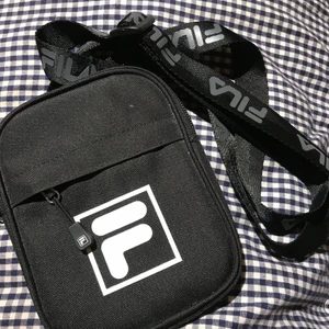 Fila pusher bag - svart Pusher bag från Fila med märke på framsidan, väskan har tre stycken fack och justerbart axelband med text på, väskan är köppt för ca två år sen men den är aldrig använd! Nypris:250kr