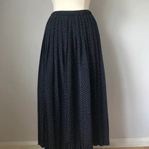 Plisserad långkjol - Marinblå plisserad långkjol med vita prickar och resår i midjan. Plagget är i mycket gott skick och har storleken 44. 