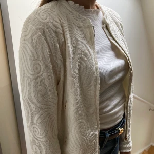 Vit jacka - Gräddvit jacka med fina mönster! Jackan stängs med dragkedja och har även två fickor med dragkedja. Har bara använts en gång!🌼