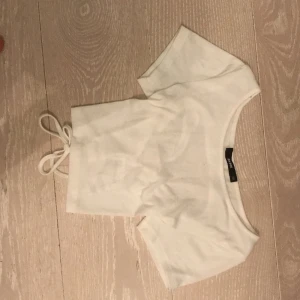 En fin vit kortärmat tröja som även är lite magtröja som är korsad där bak - Storlek:xs/s   Den har aldrig andvänts och är i bra skick. Frakten ingår i priset.