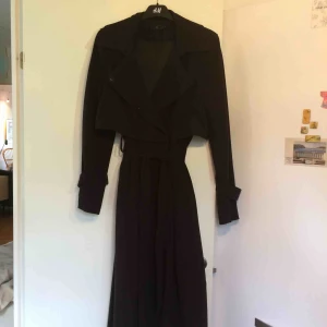  - Svart ankellång trenchcoat i mjuk polyester och viskos. 