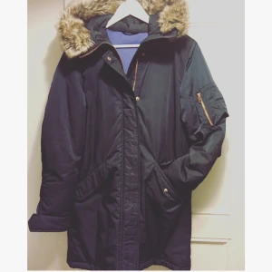  - Safirblå Filippa K parkas med fina bomberdetaljer i koppar. Superfin faux pälskrage, dragsko i midjan och snyggt blått foder. Varm, lätt, polyesterfodrad. Använd en halv säsong, jättefint skick. Storlek S men passar en M. Nypris 3500 sek. 