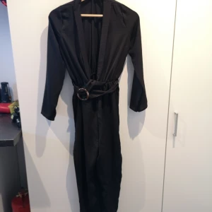 Boohoo lång svart byxdress - I mycket bra skick. Använd endast en gång. Storleken är i petite size, alltså anpassad för de som är under 160 cm. Jättefin byxdress men kände att den inte kom till användning så mycket så vill sälja denna underbara byxdressen! 