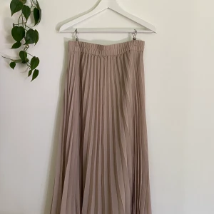 Plisserad kjol, Monki - Ljusbeige plisserad kjol. Går ungefär till vaderna på mig som är 165cm lång. Resår i midjan. Använd fåtal gånger. Frakt tillkommer (59kr)