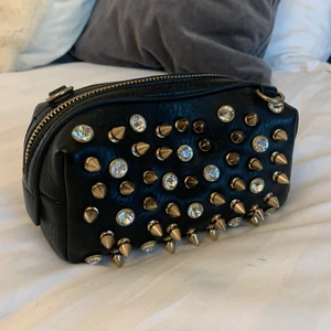 Väska - Mindre väska med nitar och stenar på, samt avtagbara band så går att använda som clutch. Aldrig använd så helt ny 
