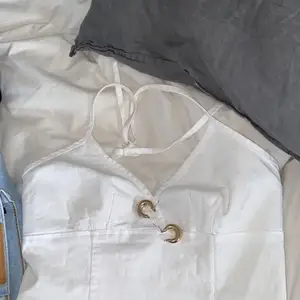 Ett vit gullit linne i mjukt jeans tyg som tyvär inte används. Öppen rygg och knutte i nacken 