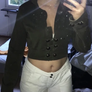 Grön kofta.  - Militärgrön kofta/croppad hoodie som jag köpt på second hand. Storlek m och från ett märke som heter vila. Kan knäppas där framme med knapparna. 