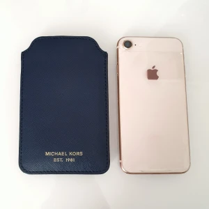 MK mobil case navy - Färg: navy.  Mått: 13,5 x 8,5 cm.  Passar: • iPhone 6, 7, 8 • Även äldre, iPhone 4 & 5 >På bilden ligger en iphone 8. Original Michael Kors fodral, fr Jackie. Använd fåtal gånger. fint skick. Fodral m tyg av logo MK. Tåligt material. (Nypris: 499 kr)