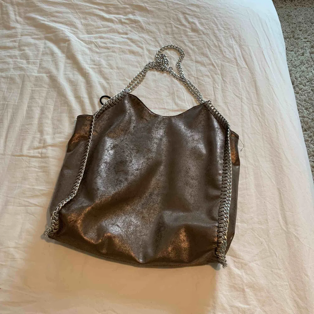 En oäkta stella mccartney väska köpt på minto i en fin brun glänsande färg! Den är ca 35 ca på bredden, och ca 30 på längden. Har inget långt band i mitten.. Väskor.