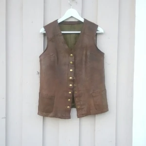  - Skinnväst i unisexmodell. Robusta knappar, små fickor och välskött läder. 