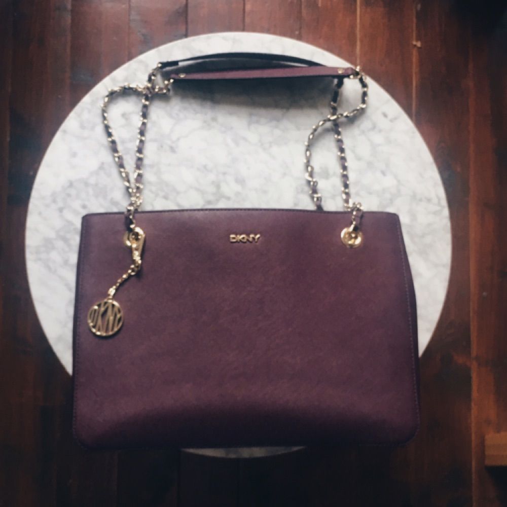 Äkta DKNY Purple Saffiano Burgundy Medium Tote Bag. Jättesvår färg att fånga på bild men den är mörklila, på sista bilden ser den nästan svart ut pga ljuset, men ville bara visa att den är i bra skick! Använd fåtal gånger, inga revor eller märken på väskan! Flera fack inuti och DKNY mönstrat foder. Gulddetaljer på kedjan och hänget vilket knappt syns men skickar jättegärna fler bilder vid förfrågan! Säljer pga inte riktigt min stil längre, nypris €236 men är villig att diskutera pris! Köpare står för eventuell frakt . Väskor.