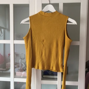  - Senapsgul croptop med coldshoulder-cut. Den har en halvpolokrage och är i lite ribbat material 🐥