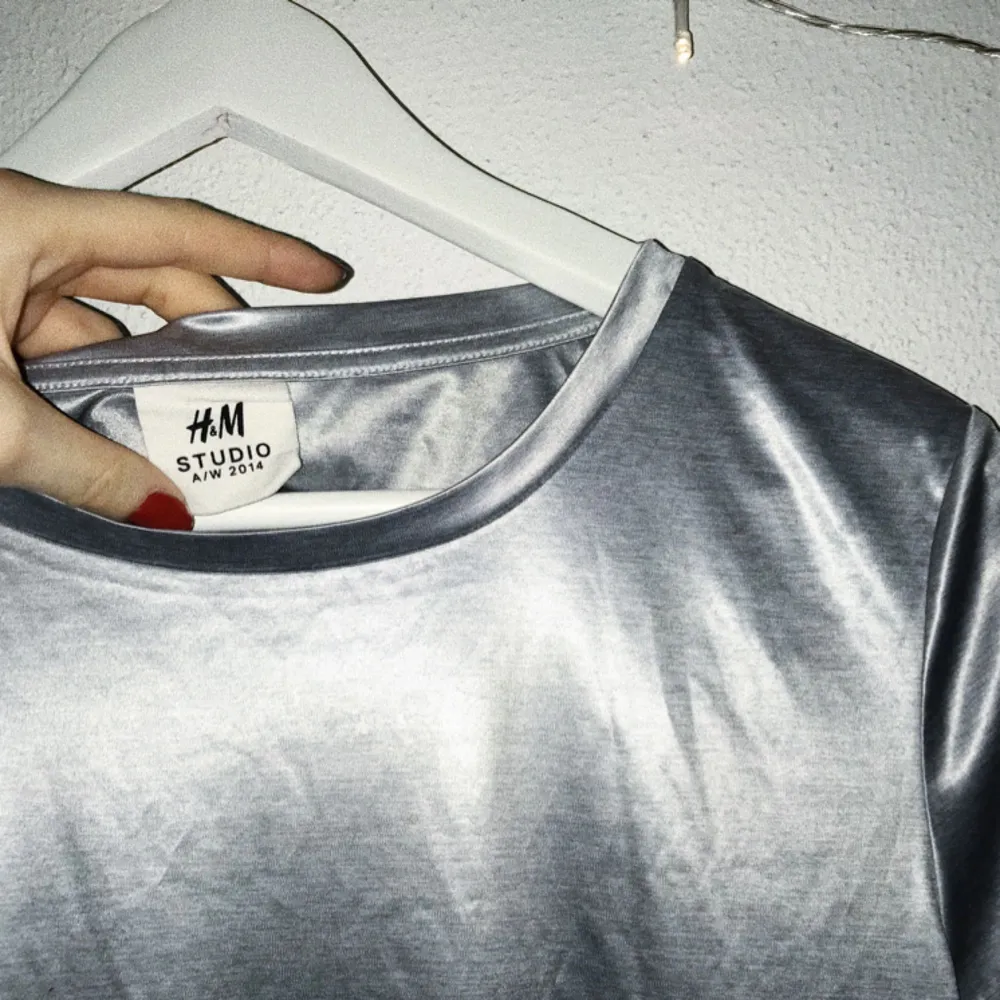 Silvrig t-shirt från H&M STUDIO. Såld för kvinnor men fungerar unisex.  Om kund bor utanför Lund/Malmö får den stå för pris av frakt <33. T-shirts.