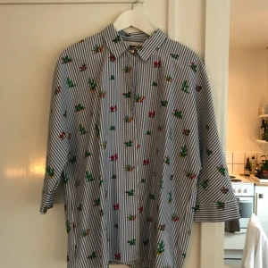  - Ljusblårandig skjorta med kaktusar på. Använd en gång, har en slits i ryggen och trekvartsärm. Möts upp i Sthlm eller skickar mot fraktkostnad. 