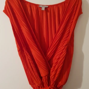 Röd plisserad omlottopp L XL - Fin röd plisserad omlottopp med knytband.stor i stl mer som XL. Fint beg skick. Djur finns i hemmet. Fraktpriset är ca pris 