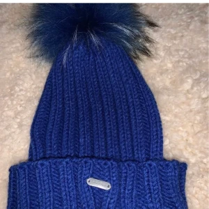 Tiff-tiffy mössa - Säljer en blå tiff-tiffy mössa som endast är använd 1 gång🦋 äkta tvättbjörnspäls på tofsen🌸 säljer för 300kr OBS Pris kan diskuteras✨
