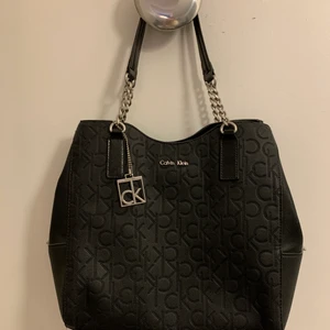 Calvin Klein handväska - En klassisk och elegant väska - perfekt för alla tillfällen. Alldeles lagom storlek för både vardag & finare tillfällen. (Material: 100% polyuretan). Calvin Klein metall logotyp på framsidan. 