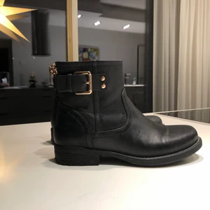 Skor - Svart skor i fake läder med ludd inuti. Har guld spännen som detaljer.