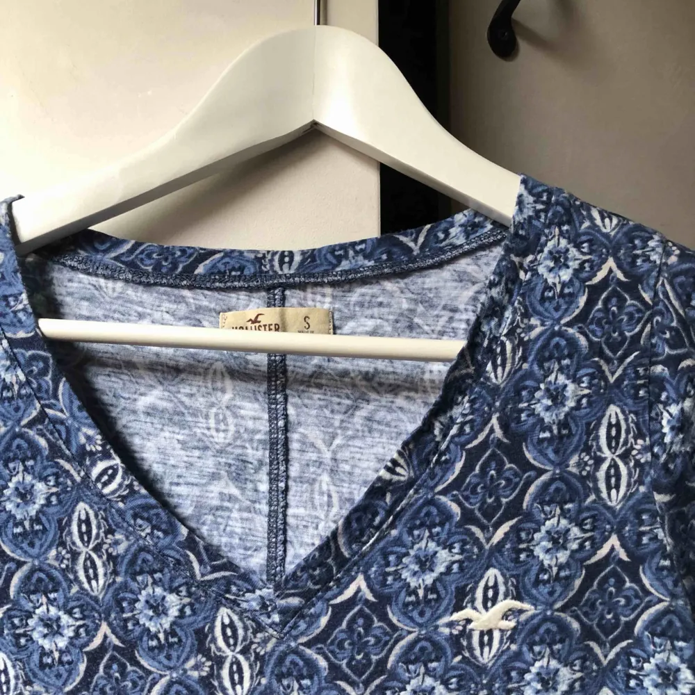 Blå mönstrad t-shirt med v-formad hals från Hollister. Köpt i London 2013, använd ca 5 ggr, i bra skick! Köparen står för frakten, swish🌷 . T-shirts.