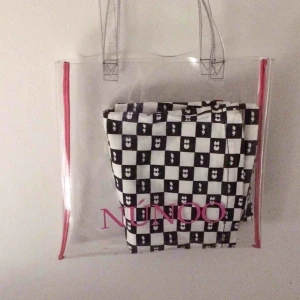  - Superfin transparent märkesväska med rosa text från Núnoo. 