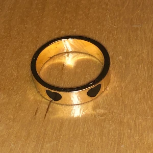 Guldfärgad ring - Guldfärgadring med tre svarta hjärtan på. Storlek 6-8. Aldrig använd! Kan skicka fler bilder vid intresse. Köparen står för frakt