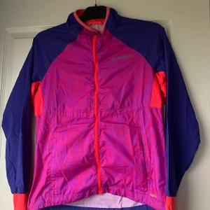Vindjacka  - En färgglad vindjacka från soc i bra skick. Går att spänna in längst ner och är väldigt skön att träna i. Reflexer lite överallt. Hör av er vid frågor eller fler bilder✨