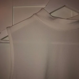 Vit blus med hög krage  - Vit blus med hög krage utan ärmar från Cubus. Knappt använd. Knappar i ryggen.  
