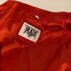 Rött set i skinn - Ett rött set med kjol och jacka/kavaj i rött skinn! Kjolen har dragkedja och tryck-knapp baktill och även slits. Jackan är lite fälld på ärmarna som syns på bild 3, men själva setet i sig är knappt använt. Det är fodrat och passar perfekt till något ex ett basplagg!    Bra kvalite och extraknapp till jackan finns medsytt på insidan.