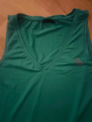 Grön linnetopp från Adidas - Snygg grön linnetopp från zizzi med v-ringning och ärmlös design. Perfekt för träning eller sommarhäng. Tillverkad i mjukt och lätt polyester för maximal komfort.