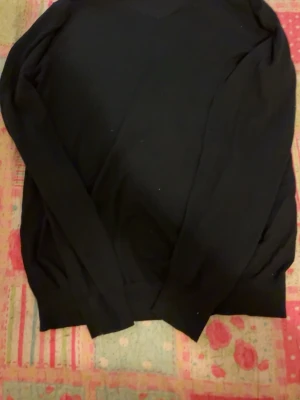 Svart V-ringad tröja Dressmann - Klassisk svart tröja från Dressmann i mjuk supima bomull. V-ringad modell med långa ärmar och ribbade muddar vid ärmslut och nederkant. Perfekt basplagg för en clean och stilren look.