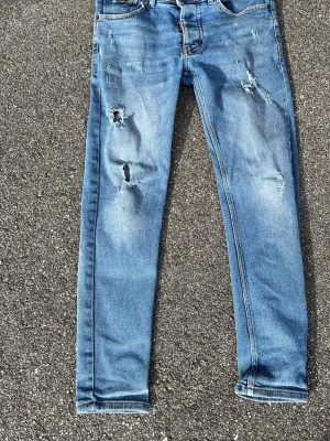  Dsquared2 jeans blå - Säljer ett par blå jeans från Dsquared2 med skinny fit och slitningar på både lår och knän. Klassisk femficksmodell med knappgylf och snygga detaljer. Priset kan diskuteras 