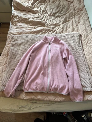 Rosa fleecejacka från Everest - Mysig rosa fleecejacka från Everest med hel dragkedja framtill och hög krage. Jackan har broderad logga på bröstet och är tillverkad i mjukt fleecematerial. Perfekt för lager-på-lager och chill dagar.